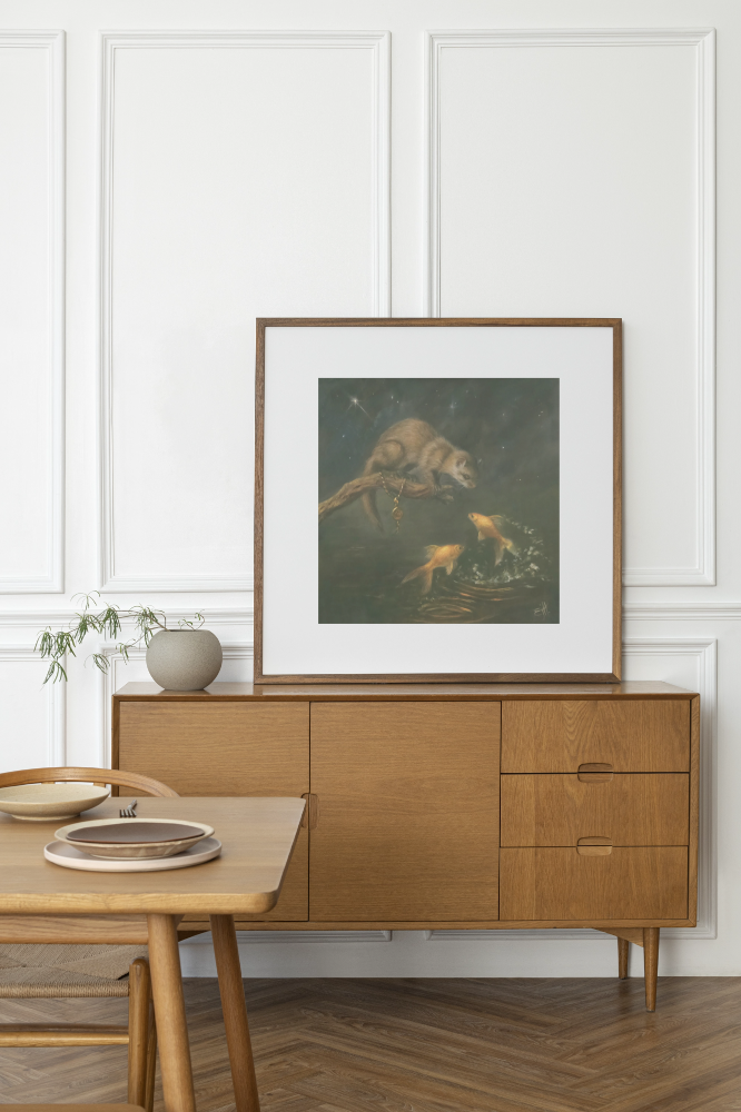 A framed art print depicting a pine marten and goldfish, styled on a wooden sideboard in a modern room setting.