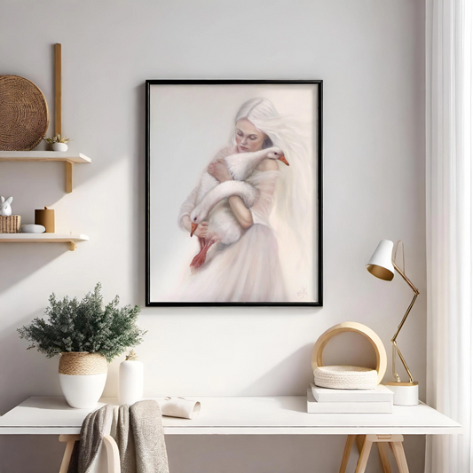 A framed art print depicting a woman in a white dress holding a white goose, displayed on a light gray wall above a styled white desk with a lamp, books, and a plant.